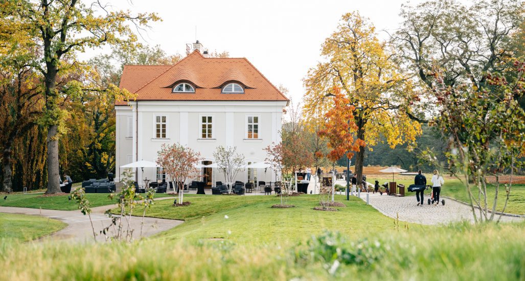 View of two golfers walking towards Nebřenice Chateau at PGA National Czec Republic at Oaks Prague