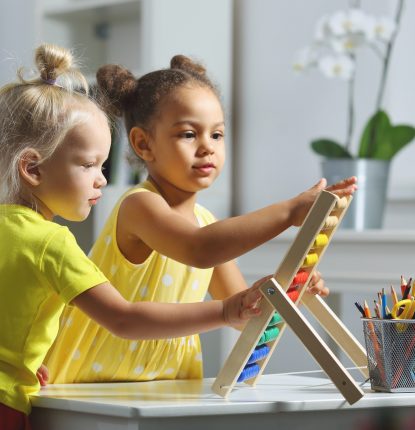 White and Black children sit together at the table and count on the abacus and smiles. Math lesson in elementary school